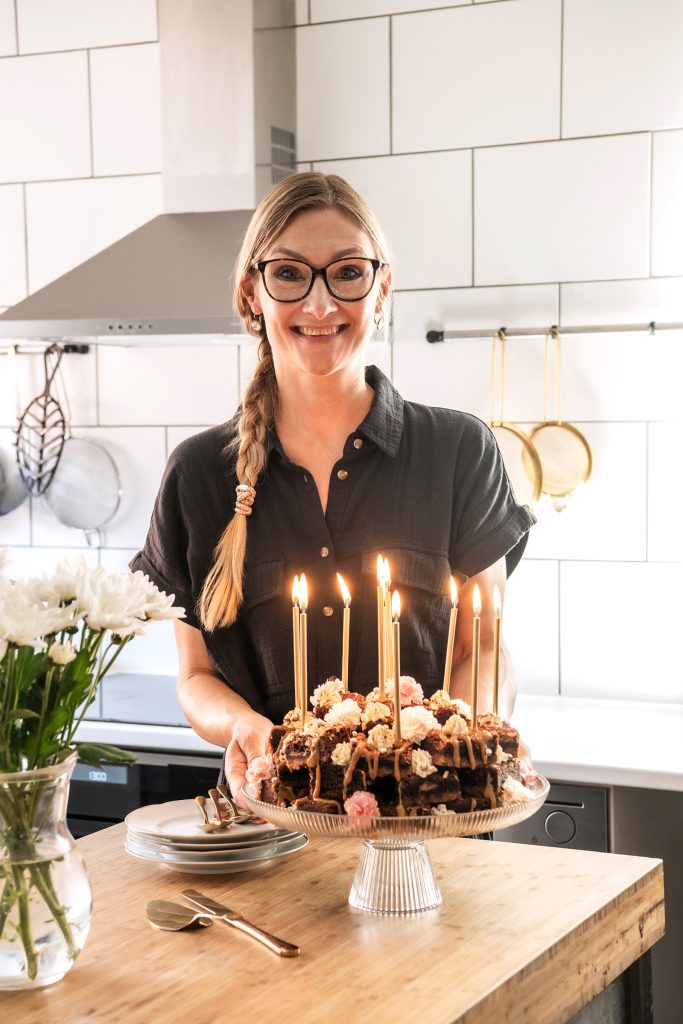 Teresa Välimäki seisoo keittiössä käsissään leipomansa Maapähkinä-suklaabrowniekakku.